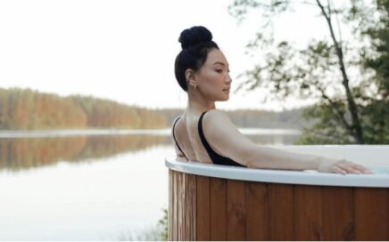 Person relaxing in an outdoor hot tub by a serene lake.