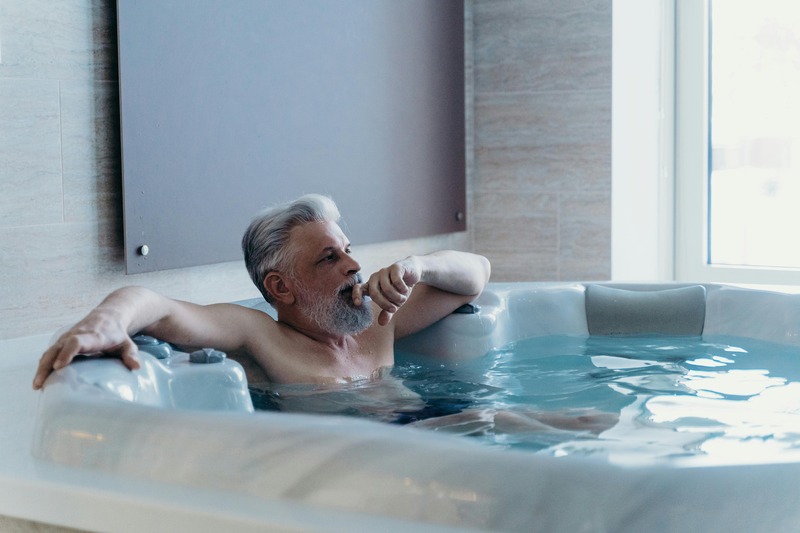 Elderly man relaxing in a hot tub indoors.